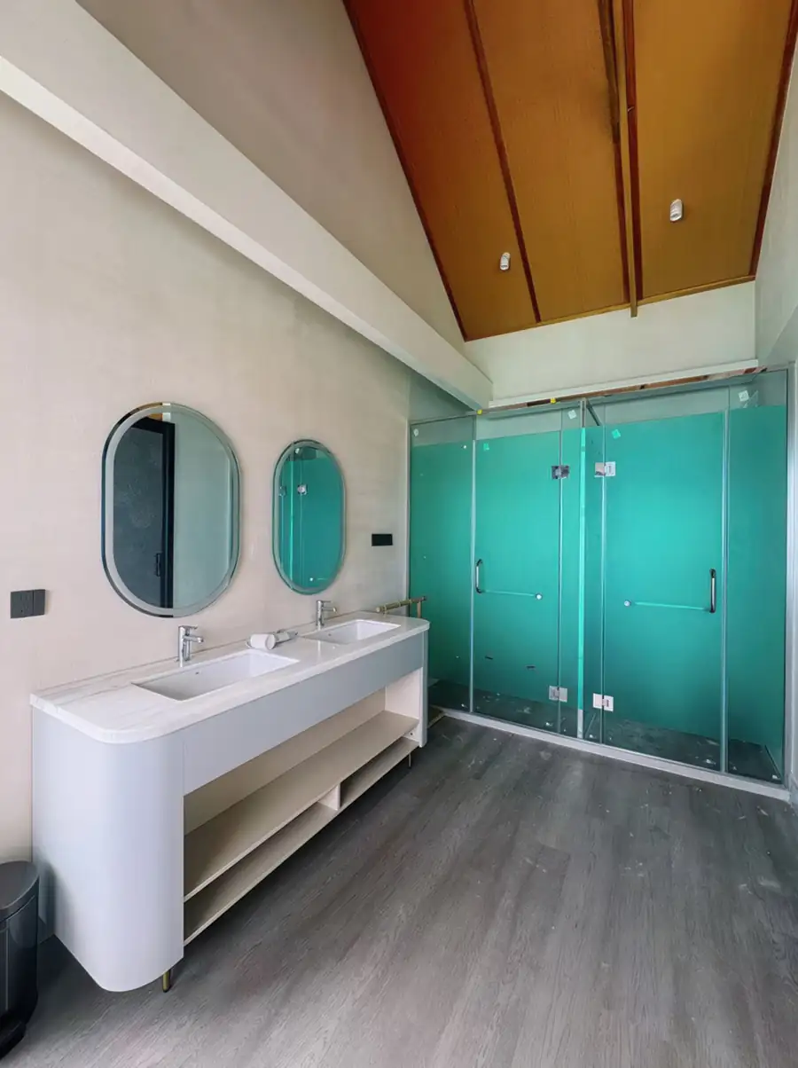 A contemporary bathroom at Cupid Resort featuring striking geometric floor tiles, a sleek vanity setup, a modern toilet, and a dedicated glass shower stall equipped with an electric shower.