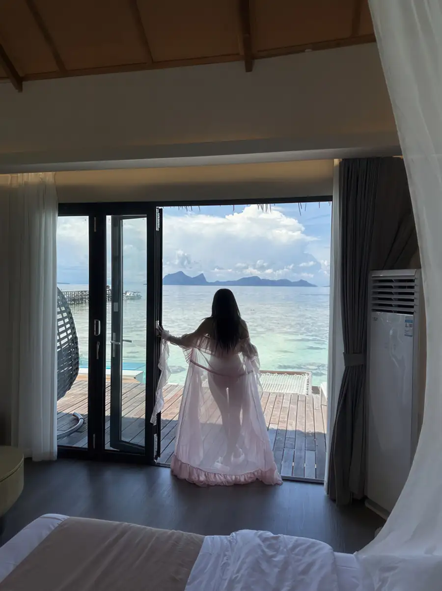 A modern bedroom at Cupid Resort on the Celebes Sea featuring a large bed facing panoramic glass doors with direct access to the private balcony, timber floors, and air con.