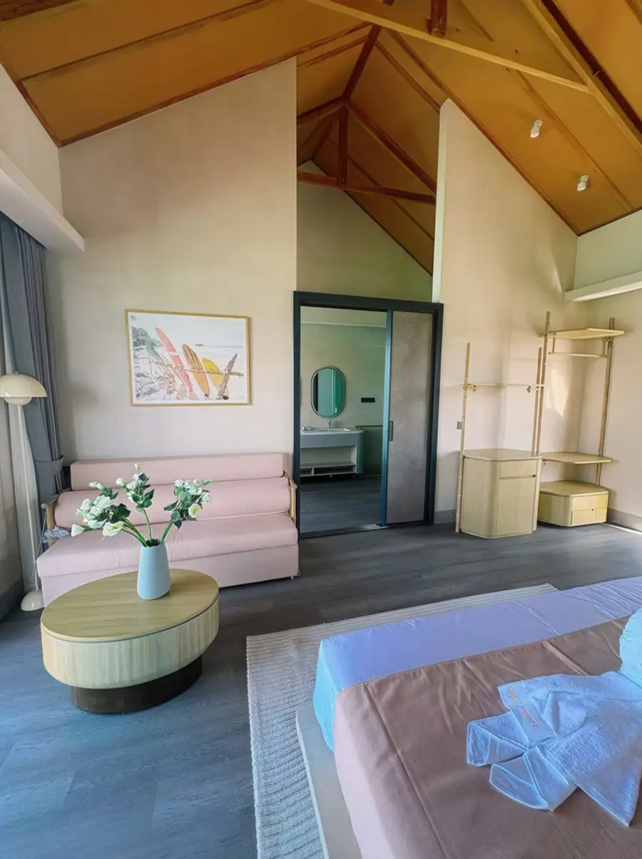 A serene bedroom at Cupid Resort near Semporna showcasing a king size bed, a traditional style wooden vanity, sleek wooden floors, air con, and a large window overlooking an overwater net.
