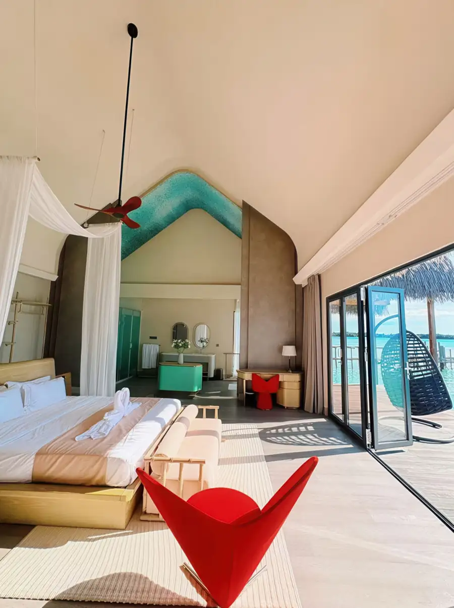 A bright bedroom at Cupid Resort on the Celebes Sea featuring a large bed facing seamless glass doors opening onto the private balcony, rustic timber floor with smooth wooden boards, and AC.