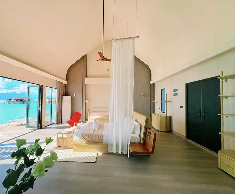 A contemporary bedroom at Cupid Resort near Semporna with a large canopy bed facing the sea, modern style decor, authentic wooden floors with glossy hardwood floors, and air conditioning.